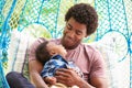 Father With Baby Son Relaxing On Outdoor Garden Swing Seat