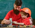 Father with beard and little son in classroom teaching to use tools, chalkboard on background. Mens work concept. Boy