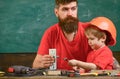 Father with beard teaching little son to use tools in classroom, chalkboard on background. Mens work concept. Boy, child