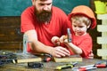 Father with beard teaching little son to use tools, hammering, chalkboard on background. Handyman concept. Boy, child