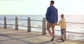 Father, boy and holding hands on promenade, beach or walking on vacation with love, care and bonding. Man, child and
