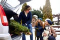 Father brought christmas tree in large trunk of SUV car. Daughter, mother and dog meet dad happily help him with