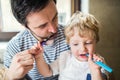 Father brushing his teeth with a toddler boy at home.