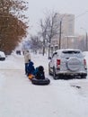 A father carries his three children on a steam train of sledges and two airbags along a snowy winter street in a