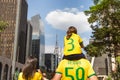 Father carrying his daughter on his shoulders, both wearing green and yellow T-shirts representing the colors of the Brazilian