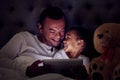 Father and child in bed with tablet reading ebook or to watch a film together at night. Happy girl with her dad enjoying Royalty Free Stock Photo