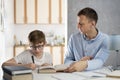 Father and child are doing homework.Young teacher tutor is studying with boy.Boy teenager in glasses writes in notebook Royalty Free Stock Photo