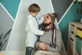 Father and child playing clinic and doctor, little boy in medical gown with stethoscope treats dad