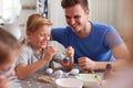 Father With Children Sitting At Table Decorating Eggs For Easter At Home