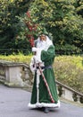 Father Christmas robed in green, masked and carrying holly branc