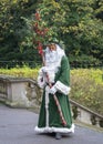 Father Christmas robed in green, masked and carrying holly branc