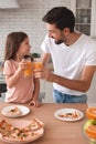 Father clicking glasses with orange juice with daughter in the kitchen