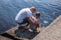 A father is crouched by his daughter at water& x27;s edge, conversation shared. Suggests guidance, care, and family