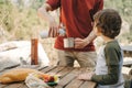 Father dad pours hot coffee tea from thermos into the mug on a family picnic in the mountains. Child school boy kid is Royalty Free Stock Photo