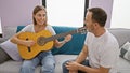 Father and daughter bonding while sitting on the sofa at home, playing classical guitar; their casual expressions radiate love and Royalty Free Stock Photo