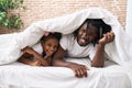 Father and daughter covering with bedsheet lying on bed at bedroom