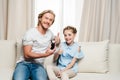 Father and daughter holding medicine and showing thumbs up while sitting together on sofa Royalty Free Stock Photo