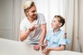 Father and daughter holding pill and glass of water while smiling each other at home