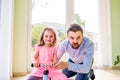 Father and daughter playing together, riding a bike indoors Royalty Free Stock Photo