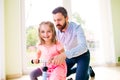 Father and daughter playing together, riding a bike indoors Royalty Free Stock Photo