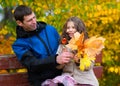 Father and daughter portrait in an autumn park. Happy people pose against the background of beautiful yellow trees. They sit on a Royalty Free Stock Photo