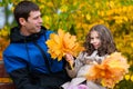 Father and daughter portrait in an autumn park. Happy people pose against the background of beautiful yellow trees. They sit on a Royalty Free Stock Photo