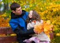 Father and daughter portrait in an autumn park. Happy people pose against the background of beautiful yellow trees. They sit on a Royalty Free Stock Photo