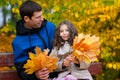 Father and daughter portrait in an autumn park. Happy people pose against the background of beautiful yellow trees. They sit on a Royalty Free Stock Photo