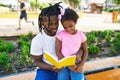 Father and daughter reading book sitting together on bench at park Royalty Free Stock Photo