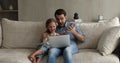 Father and daughter sit on couch watching cartoons on laptop
