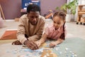 Father and daughter solving jigsaw puzzle lying on soft carpet at home