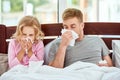 Sick family. Father and daughter suffering from flu or cold and wiping noses while lying in bed together at home. Virus