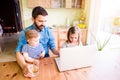 Father and daughters, playing on laptop, sitting in kitchen Royalty Free Stock Photo