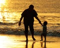 Father and dauther holding hands and playing at the beach in Bali, Indonesia during a golden sunset. Ocean like gold.