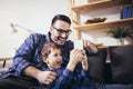 Father embraces little son family sitting on couch at home using smart phone feels happy cheerful laughing on funny videos Royalty Free Stock Photo
