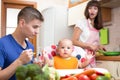 Father feeding his baby while mother cooking at kitchen