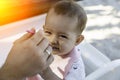 The father feeds his 8 month old daughter with a spoon. Baby with sly face is sitting in a chair at a table on the beach at sunny