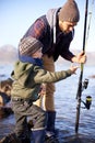 Father, fishing and teaching for young boy, rocks and bonding for activity by ocean. Sea, rod and learning how to fish Royalty Free Stock Photo