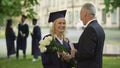 Father giving flowers to his graduate daughter, congratulations, paternal pride