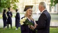 Father giving flowers to his graduate daughter, congratulations, paternal pride