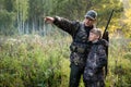 Father with gun showing something to son while hunting on a nature. Royalty Free Stock Photo