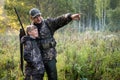 Father with gun showing something to son while hunting on a nature. Royalty Free Stock Photo