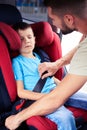 Father helps his son to fasten belt on car seat while his son is Royalty Free Stock Photo