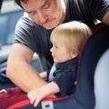 Father helps his toddler son to fasten belt on car seat Royalty Free Stock Photo