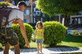 A father helps a little daughter in a yellow t-shirt put shoes on her bare feet on the hotel grounds during summer vacation.