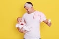 Father with his crying newborn baby posing isolated over yellow background, male tries to calm down infant and feed with milk, Royalty Free Stock Photo