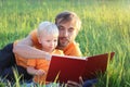 Father and his cute toddler son read book together in nature. Authentic lifestyle image. Parenting concept Royalty Free Stock Photo