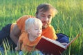 Father and his cute toddler son read book together outdoor. Authentic lifestyle image. Parenting or childhood concept Royalty Free Stock Photo