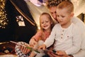 Father and his kids reading book together while sitting in handmade tent in children\'s room