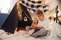 Father and his kids reading book together while sitting in handmade tent in children's room